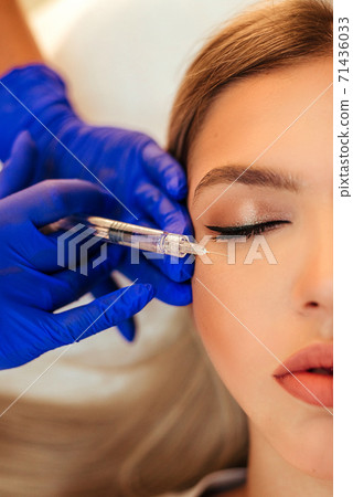 Beautiful woman gets an injection in her face. she has fashion make up and red shining lips 71436033