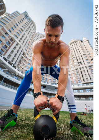 Sportive guy training with kettlebell on the background of a tall building. Sportive guy training with kettlebell on the background of a tall building. 71436742