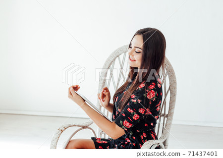 Beautiful fashionable brunette woman in a dress looks into the internet tablet 71437401