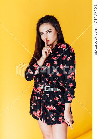 Beautiful fashionable brunette woman in a dress with flowers finger at the lips 71437451