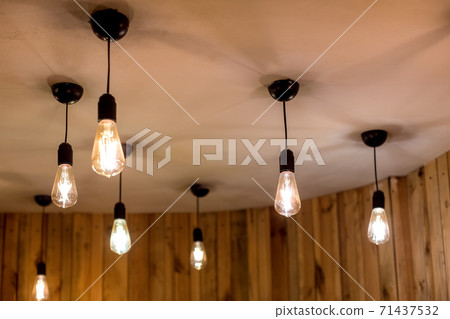 many edison bulbs hanging on a white ceiling in a room with wooden walls, retro style electric lighting in an eco friendly interior close-up of glow details, nobody. 71437532