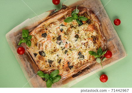 Thin crust pinsa with smoked salmon, basil and mozzarella on a green background. Traditional Italian food. Top view 71442967