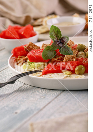 Vertical shot healthy and tasty vegan salad with watermelon, olives, fresh herbs, basil, multi-grain chips and peanut sauce. Vegetarian food. Vertical shot healthy and tasty vegan salad with watermelon, olives, fresh herbs, basil, multi-grain chips and peanut sauce. Vegetarian food. 71442971
