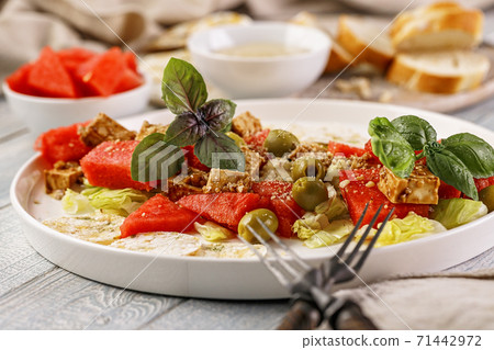 Close-up healthy and tasty vegan salad with watermelon, olives, fresh herbs, basil, multi-grain chips and peanut sauce. Vegetarian food. Close-up healthy and tasty vegan salad with watermelon, olives, fresh herbs, basil, multi-grain chips and peanut sauce. Vegetarian food. 71442972