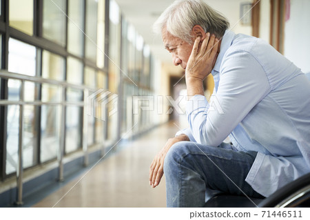sad and devastated asian senior man sitting alone in empty hospital hallway, head in hand 71446511