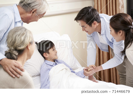 five year old asian child lying in bed in hospital ward gets a visit from parents and grandparents 71446679