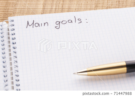 Top view workplace notebook and pen on wood table background, retro effect. Inscription - main goals. Setting new challenges for life Top view workplace notebook and pen on wood table background, retro effect. Inscription - main goals. Setting new challenges for life 71447988