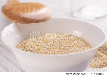 Dry oat bran in a white plate on a light wooden table with a wooden spoon. The concept of useful natural nutrition Dry oat bran in a white plate on a light wooden table with a wooden spoon. The concept of useful natural nutrition 71448002