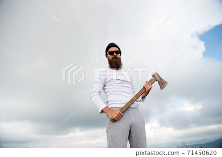 Hipster with beard on strict face holds axe, cloudy sky background. Man with beard Hipster with beard on strict face holds axe, cloudy sky background. Man with beard 71450620