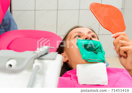 The patient holds a mirror, sits in a dental chair, examines the quality of the treated teeth. 71451419