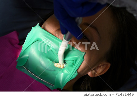 A woman at a dentist's appointment, a dentist uses a rubber dam and dental tools for treatment. 71451449