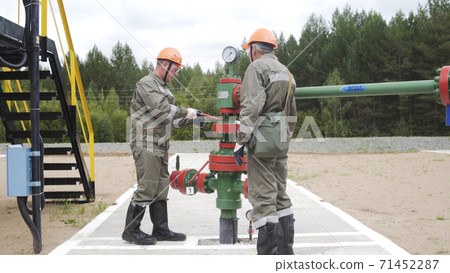 Two oil field technical workers closing valve of x-mass wellhead to shut off well. Decline in oil production after adoption of agreements at meeting of OPEC to stabilize price of oil. 71452287