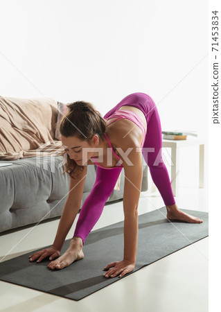 Beautiful young woman working out indoors, doing yoga exercise on gray mat at home Beautiful young woman working out indoors, doing yoga exercise on gray mat at home 71453834