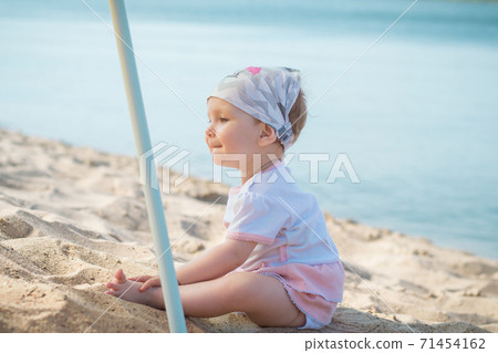 Little girl child in summer dress sits on beach beach or sea and lake and playing with yellow sand	 Little girl child in summer dress sits on beach beach or sea and lake and playing with yellow sand	 71454162