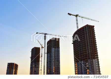 Tower cranes in action on blue sky background. Tower cranes in action on blue sky background. 71454507