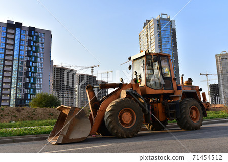 Wheel loader with a bucket on a street in the city during the construction of the road. Construction site Wheel loader with a bucket on a street in the city during the construction of the road. Construction site 71454512