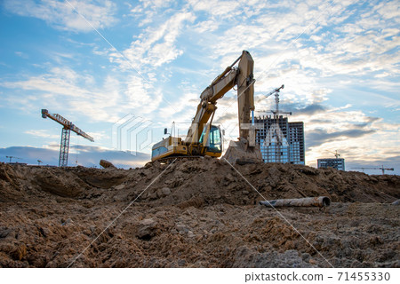 Excavator during earthmoving at construction site on sunset background. Excavator during earthmoving at construction site on sunset background. 71455330