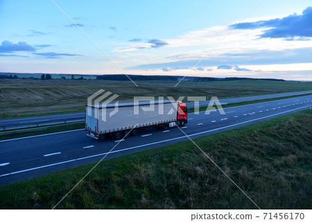 Truck with semi-trailer driving along highway on the sunset background. Truck with semi-trailer driving along highway on the sunset background. 71456170