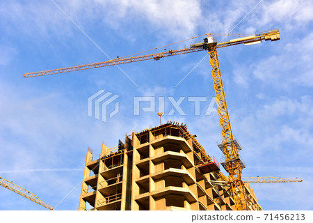 Tower cranes working at construction site on blue sky background. Tower cranes working at construction site on blue sky background. 71456213