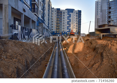 Laying heating pipes in a trench at construction site. Laying heating pipes in a trench at construction site. 71456260