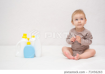 beautiful baby holding a bottle in the hand with shower gel, beside lies Baby cosmetic tubes on white isolated background beautiful baby holding a bottle in the hand with shower gel, beside lies Baby cosmetic tubes on white isolated background 71456263