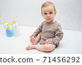 beautiful baby holding a bottle in the hand with shower gel, beside lies Baby cosmetic tubes on white isolated background 71456292