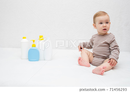 beautiful baby holding a bottle in the hand with shower gel, beside lies Baby cosmetic tubes on white isolated background 71456293