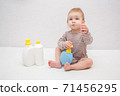 beautiful baby holding a bottle in the hand with shower gel, beside lies Baby cosmetic tubes on white isolated background 71456295