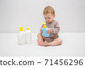 beautiful baby holding a bottle in the hand with shower gel, beside lies Baby cosmetic tubes on white isolated background 71456296