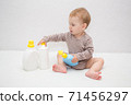 beautiful baby holding a bottle in the hand with shower gel, beside lies Baby cosmetic tubes on white isolated background 71456297