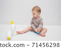 beautiful baby holding a bottle in the hand with shower gel, beside lies Baby cosmetic tubes on white isolated background 71456298