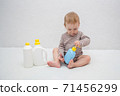 beautiful baby holding a bottle in the hand with shower gel, beside lies Baby cosmetic tubes on white isolated background 71456299