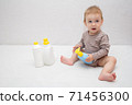beautiful baby holding a bottle in the hand with shower gel, beside lies Baby cosmetic tubes on white isolated background 71456300