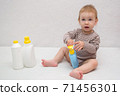 beautiful baby holding a bottle in the hand with shower gel, beside lies Baby cosmetic tubes on white isolated background 71456301