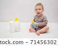 beautiful baby holding a bottle in the hand with shower gel, beside lies Baby cosmetic tubes on white isolated background 71456302