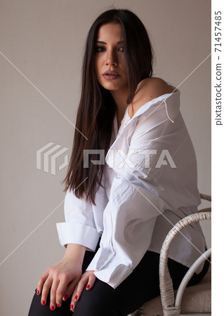 Beautiful fashionable brunette woman in a white shirt sits on a chair 71457485