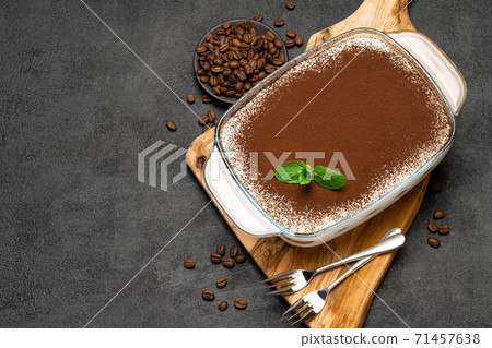 Traditional Italian Tiramisu dessert in glass baking dish on wooden cutting board on concrete background Traditional Italian Tiramisu dessert in glass baking dish on wooden cutting board on concrete background 71457638