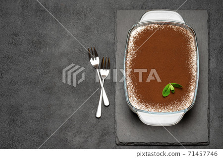 Traditional Italian Tiramisu dessert in glass baking dish on stone serving board on concrete background 71457746