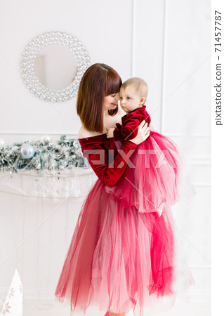 Christmas and Happy New Year Holidays. Family, mother and child concept. Tender photo of happy pretty mom holding and hugging her cute baby girl in red dress, having fun at decorated room Christmas and Happy New Year Holidays. Family, mother and child concept. Tender photo of happy pretty mom holding and hugging her cute baby girl in red dress, having fun at decorated room 71457787