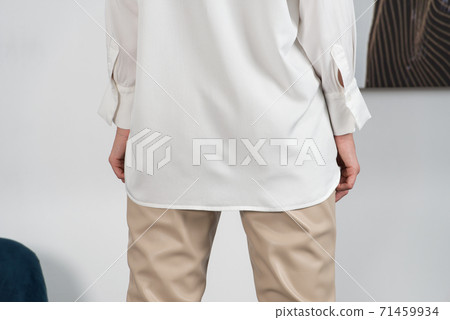 Stylish beautiful young blond woman in a tight biege pants and white shirt near a white wall in the room. Attractive girl model posing. Stylish beautiful young blond woman in a tight biege pants and white shirt near a white wall in the room. Attractive girl model posing. 71459934