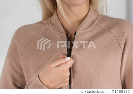 Stylish beautiful young blond woman in a biege tracksuit poses near a white wall in the room. Stylish beautiful young blond woman in a biege tracksuit poses near a white wall in the room. 71460153