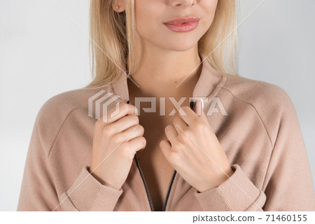 Stylish beautiful young blond woman in a biege tracksuit poses near a white wall in the room. Stylish beautiful young blond woman in a biege tracksuit poses near a white wall in the room. 71460155