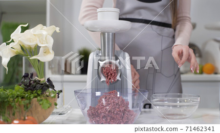 Woman puts pieces of raw meat into electric meat grinder. Pile of chopped meat. Electric mincer machine with fresh chopped meat. Preparation of minced beef with an electric meat grinder. Woman puts pieces of raw meat into electric meat grinder. Pile of chopped meat. Electric mincer machine with fresh chopped meat. Preparation of minced beef with an electric meat grinder. 71462341