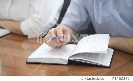 Male hand holding pen. Hand writing business report, make note on paperwork document on office desk in corporate meeting room. Man talking at group meeting about company achievement 71462371