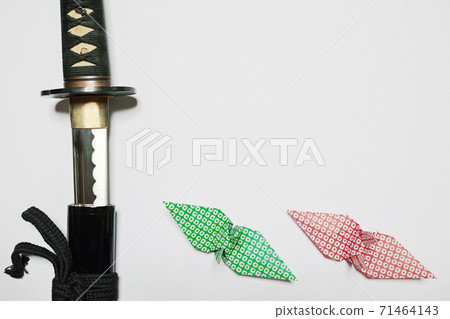 A Japanese sword placed on the left edge of white paper and a paper crane with a green and red Kanoko pattern placed below A Japanese sword placed on the left edge of white paper and a paper crane with a green and red Kanoko pattern placed below 71464143