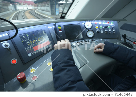 At the cabin of the passenger train. Train driver sitting in front of the dashboard and putting hand on start lever 71465442