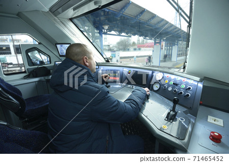 Train driver sitting in the cabin of the passenger train in front of the dashboard 71465452