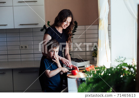 Mom and young son cut fresh vegetables to make salad in the kitchen Mom and young son cut fresh vegetables to make salad in the kitchen 71465613