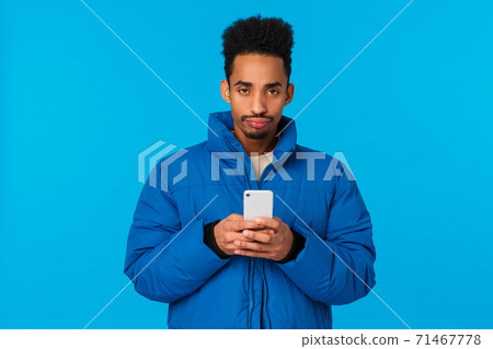 Upset and disappointed bothered african american young guy missed chance, feeling unhappy and moody, sulking frowning holding smartphone, standing padded winter jacket blue background Upset and disappointed bothered african american young guy missed chance, feeling unhappy and moody, sulking frowning holding smartphone, standing padded winter jacket blue background 71467778
