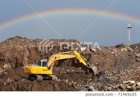 Excavator at landfill on rainbow background in sky. Disposal of construction waste and crushing Excavator at landfill on rainbow background in sky. Disposal of construction waste and crushing 71469285